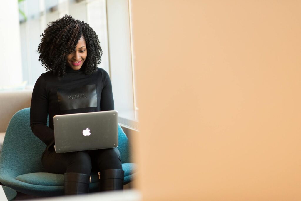 African American woman happily working on a laptop in a modern office setting.